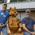 Men posing with wood carving of beaver